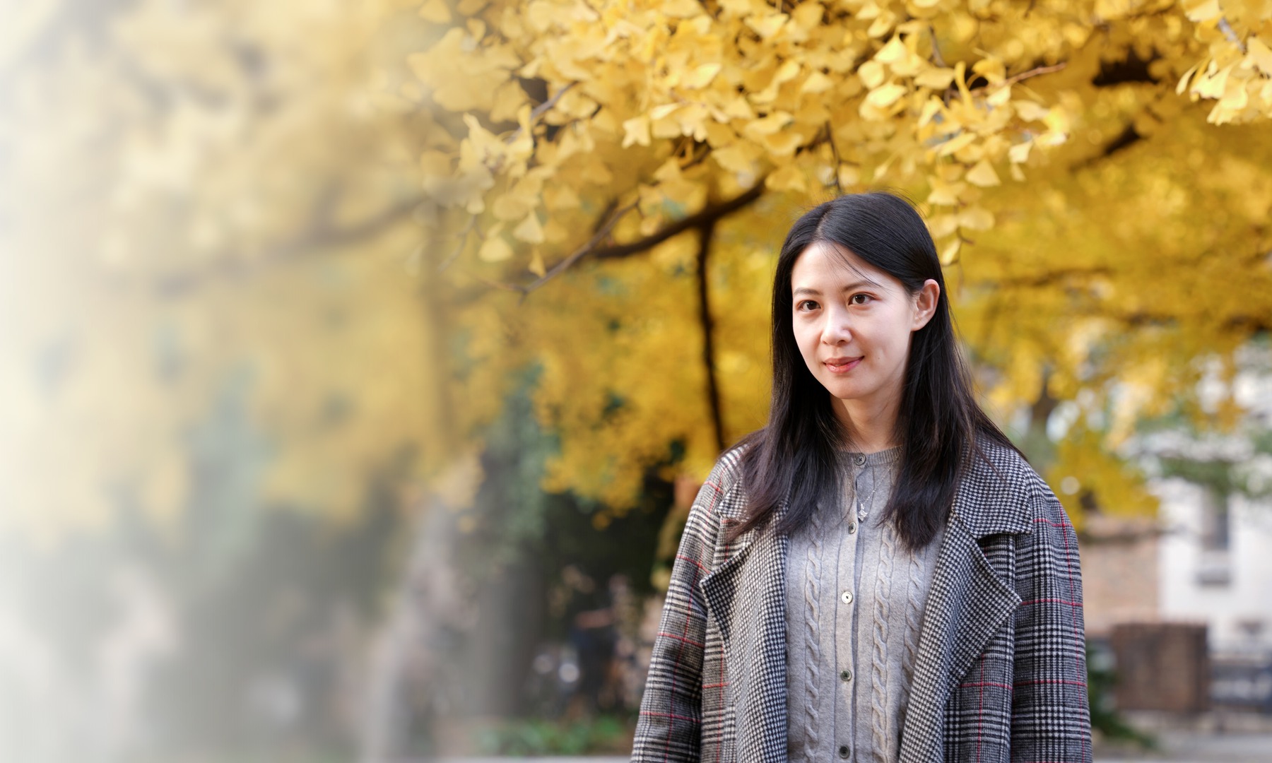 Liqiao Huang standing in front of yellow ginkgo leaves